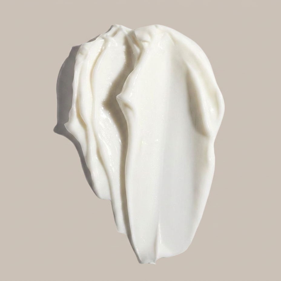 A thick, creamy white cosmetic cream swatch with soft folds and a glossy texture, set against a solid light beige background.