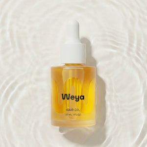 Weya hair oil bottle on a textured water background