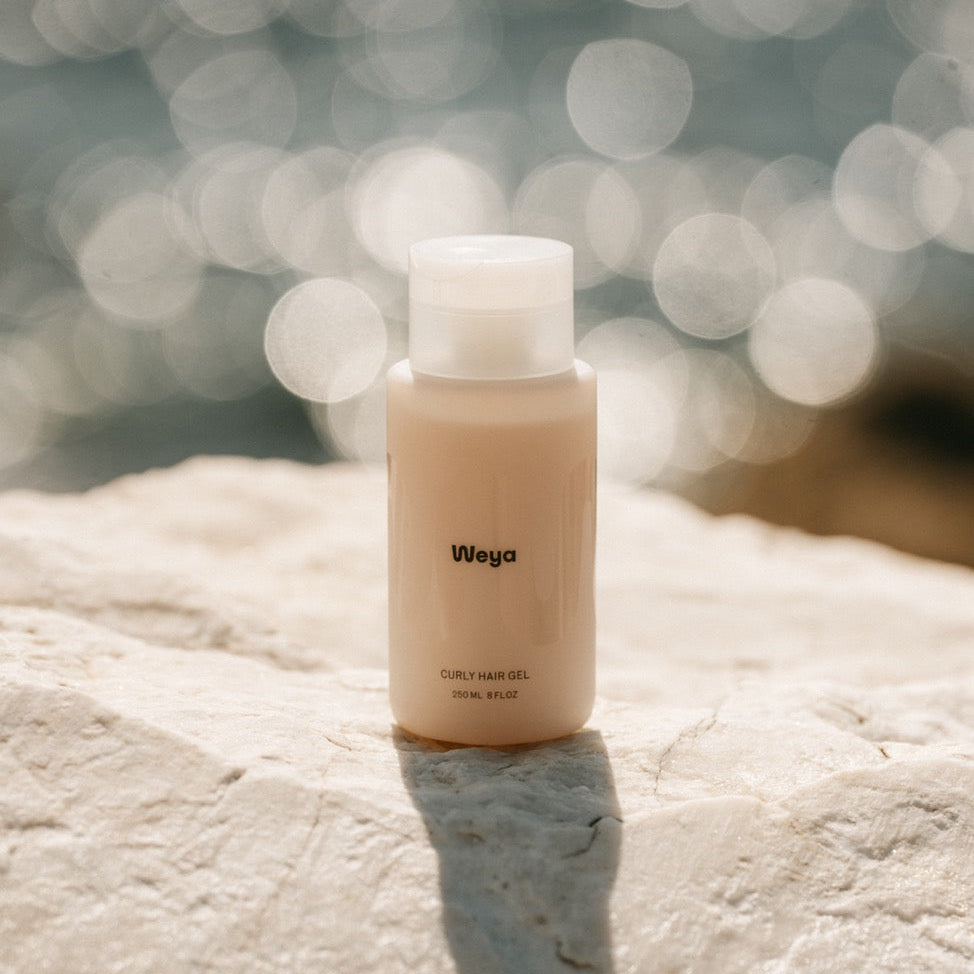 A small beige bottle labeled 'Wega' with a white cap, standing on a light stone surface with a blurred bokeh background.