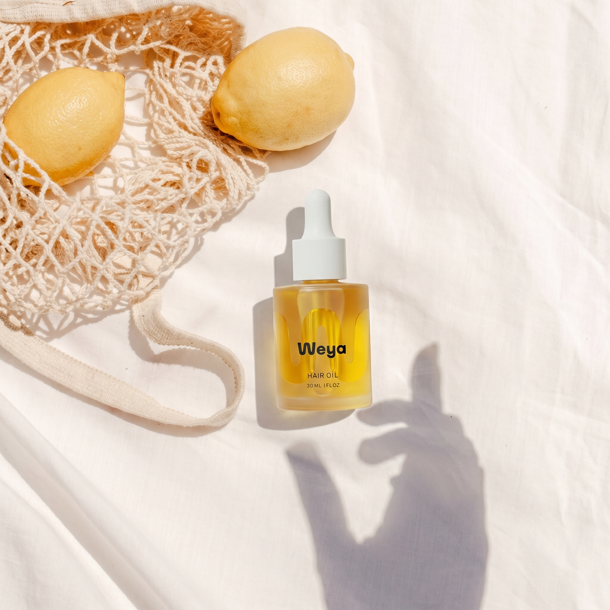 Bottle of Weya hair oil with lemons and a mesh bag on a white background