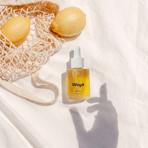Bottle of Weya hair oil with lemons and a mesh bag on a white background
