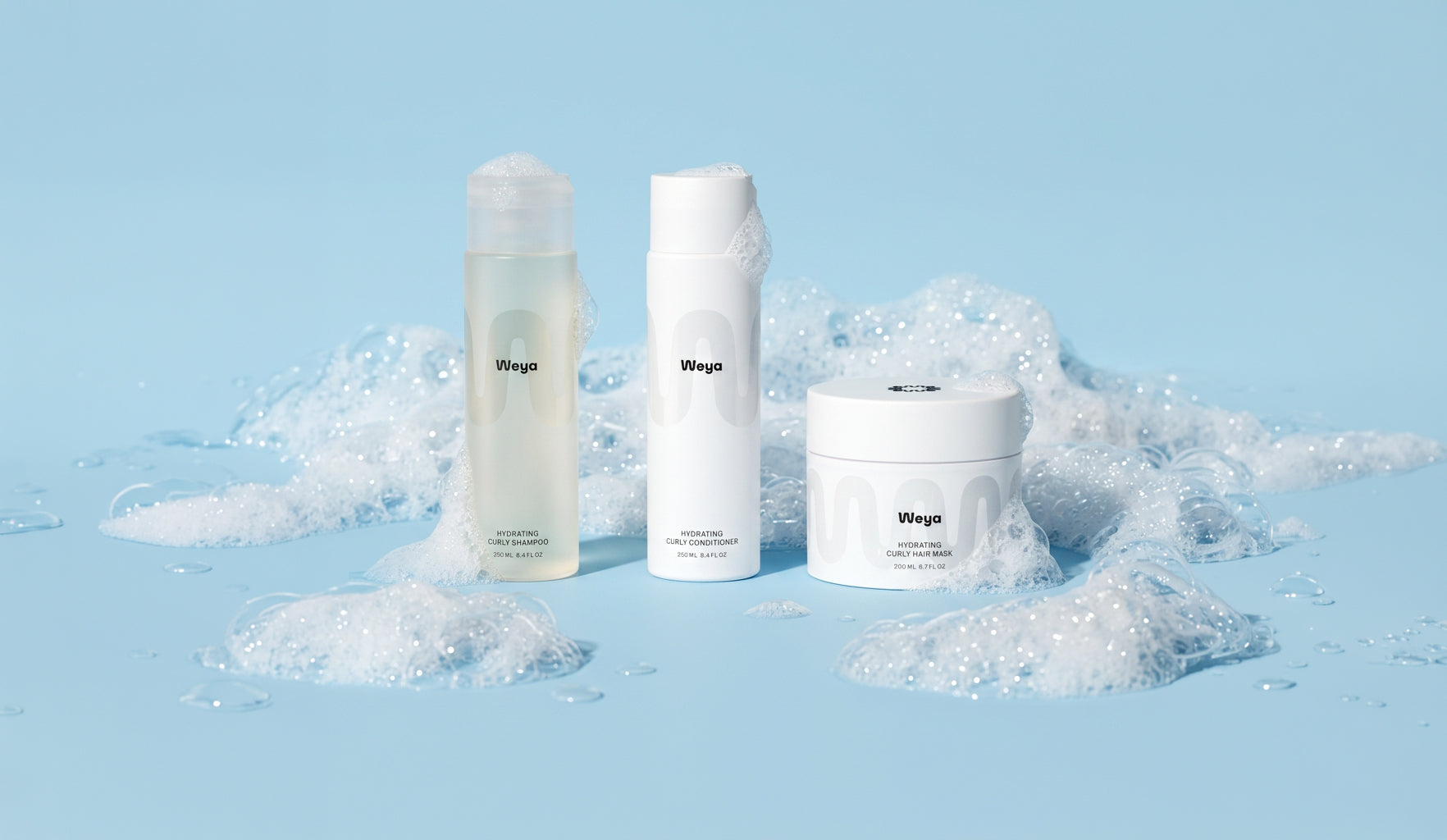 Three white skincare bottles and a white jar with the Wrigley's logo, styled on a light blue surface surrounded by white foam bubbles.